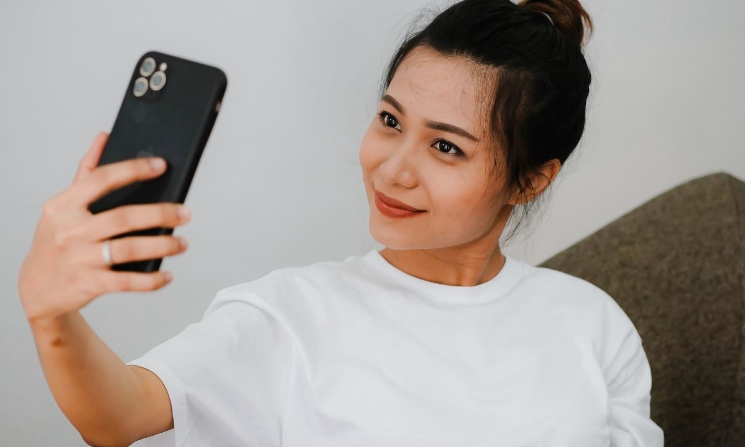 Young woman taking a passport photo selfie at home using her smartphone against a light background